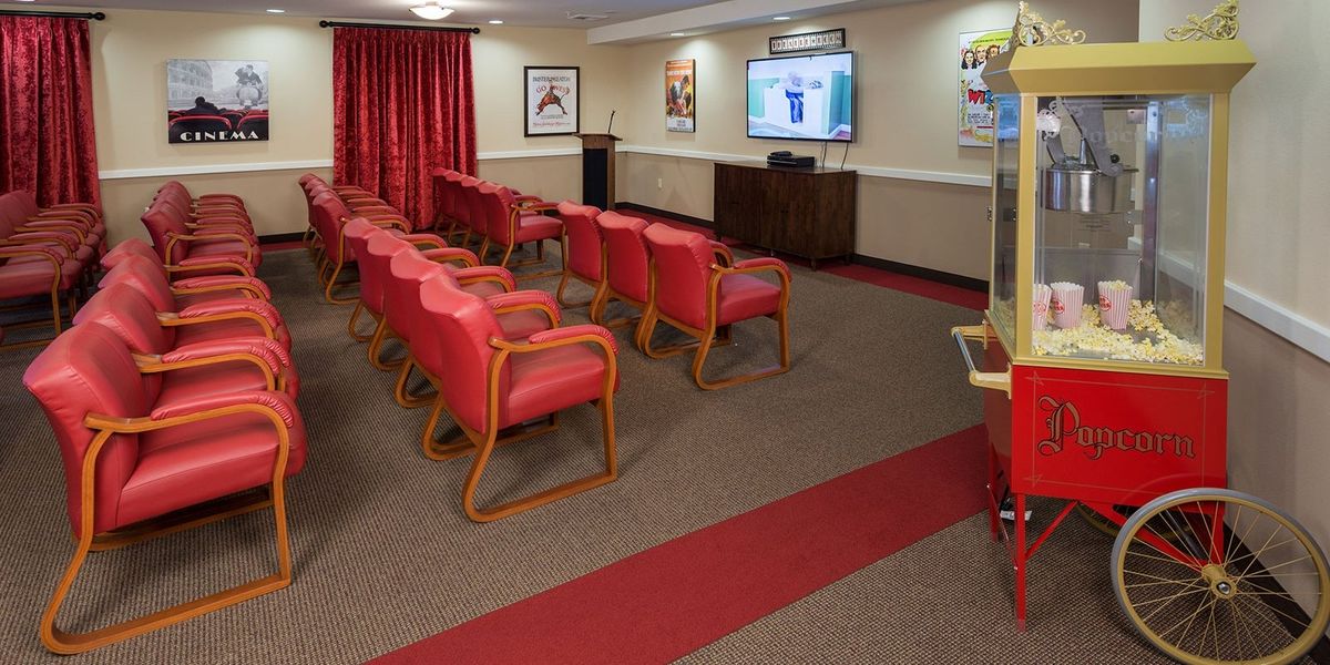 A small conference room with red chairs arranged in rows facing a presentation screen.