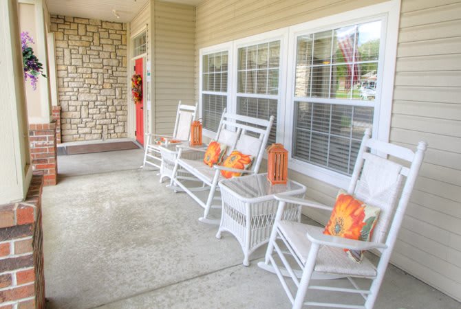A cozy porch with white rocking chairs adorned with autumn-themed cushions and pumpkin decorations.