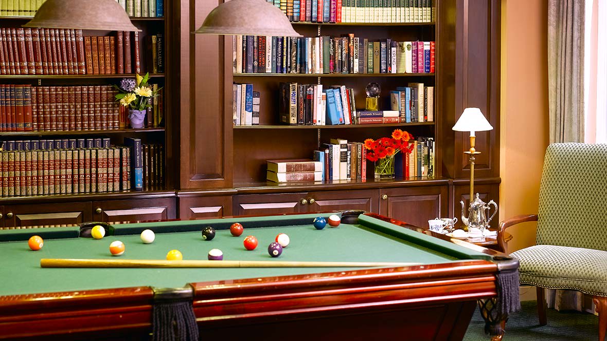 A cozy library room featuring a billiards table and a wall of bookshelves.