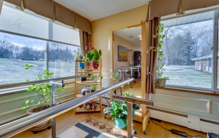 A bright rehabilitation room equipped with parallel bars and vibrant plants.
