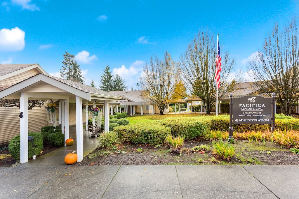 A landscaped entrance to a building with an American flag and autumn decorations.