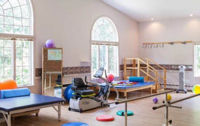 A brightly lit physical therapy room equipped with exercise machines, therapy tables, and various rehabilitation tools.