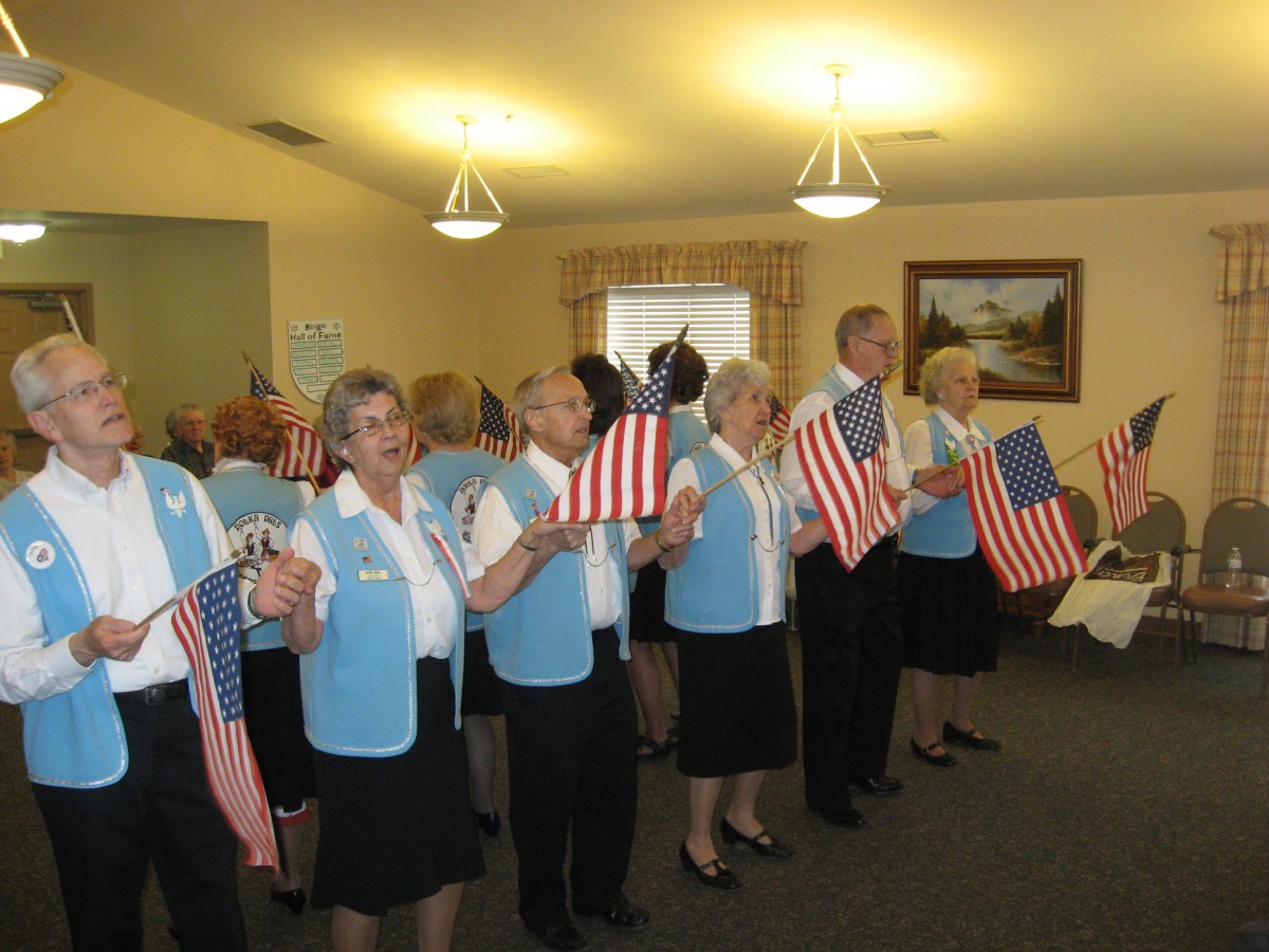 A group of seniors indoors holding American flags at a patriotic event.