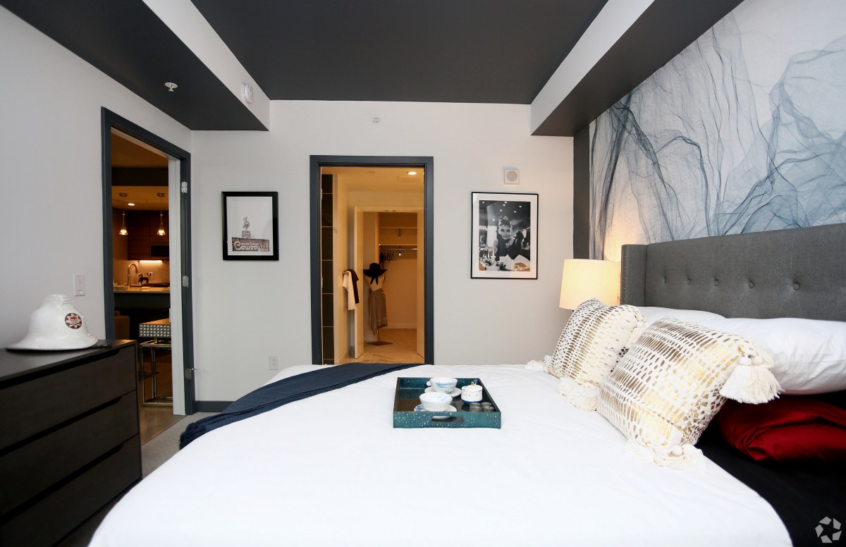 A modern hotel room featuring a neatly made bed, decorative artwork on the walls, and a tray placed on the bed.