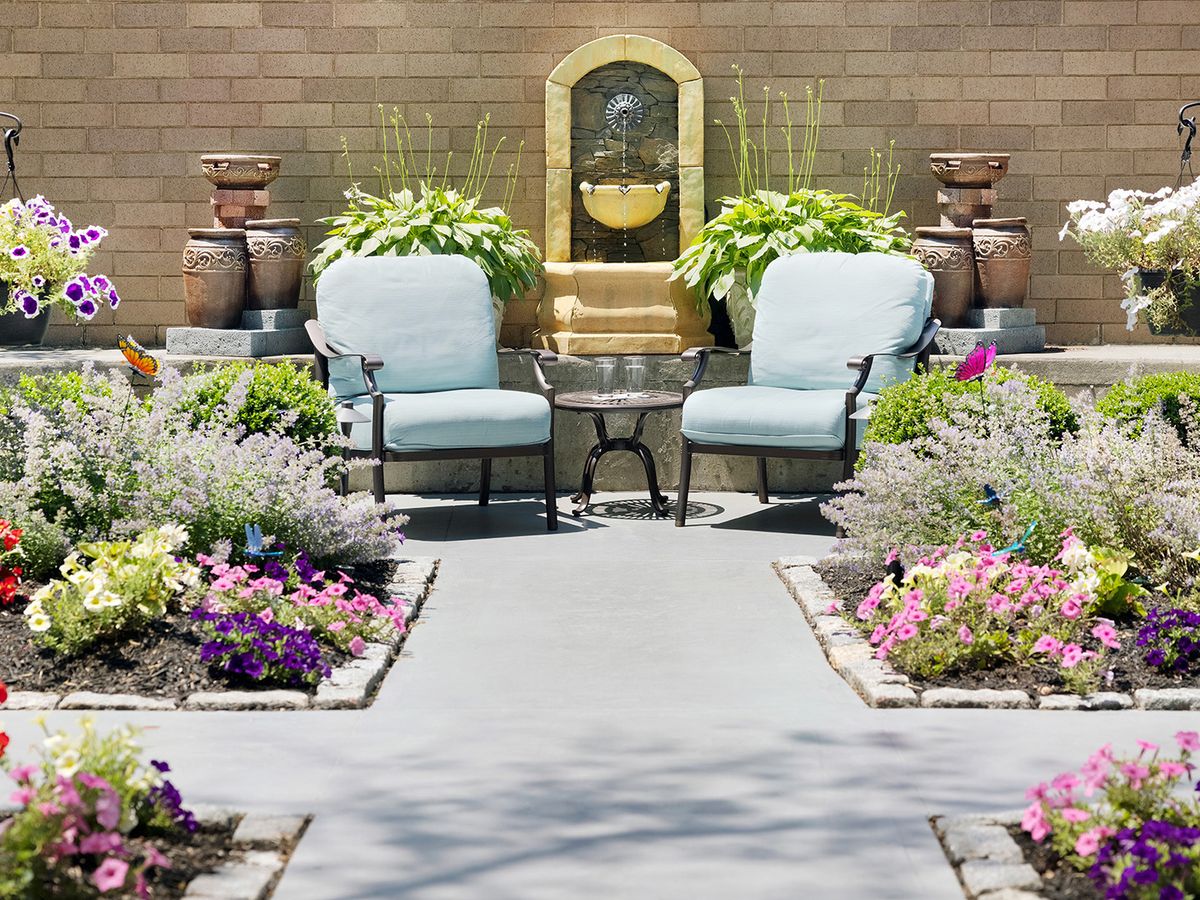 A serene garden patio with comfortable seating and a decorative water fountain surrounded by vibrant flowers.