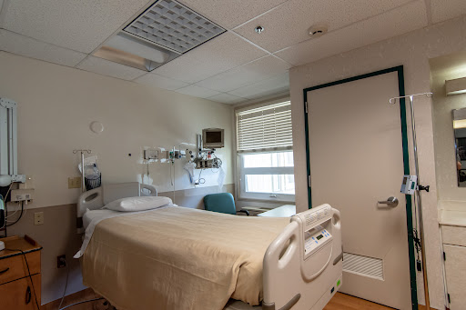 A view of a hospital patient room featuring a bed, medical equipment, and natural light coming through the window.