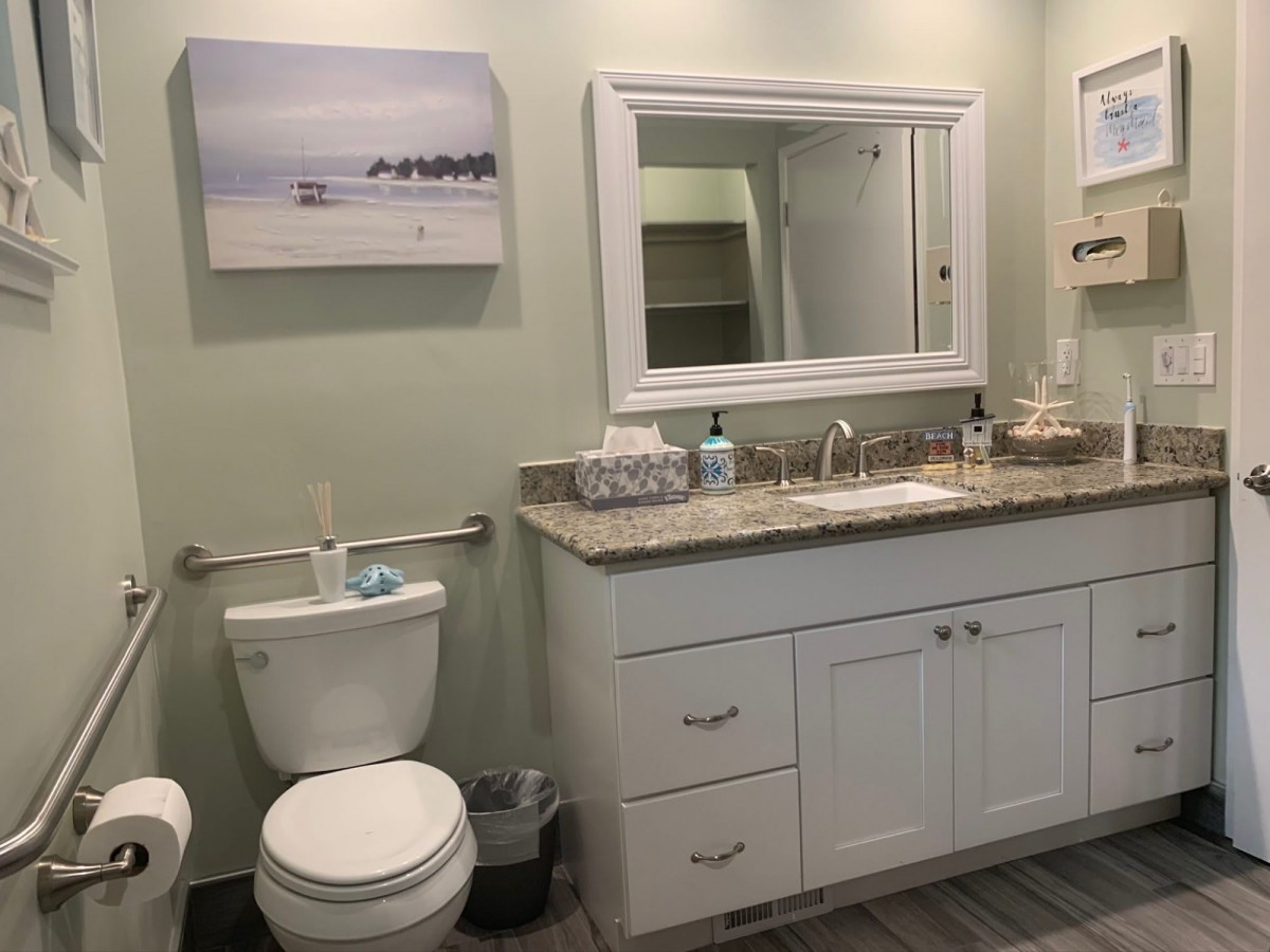 A modern bathroom featuring a white vanity with a granite countertop, a large mirror, and tasteful artwork on the wall.