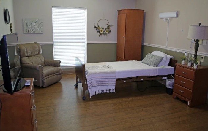 A simple hospital room with a bed, chair, and wardrobe.