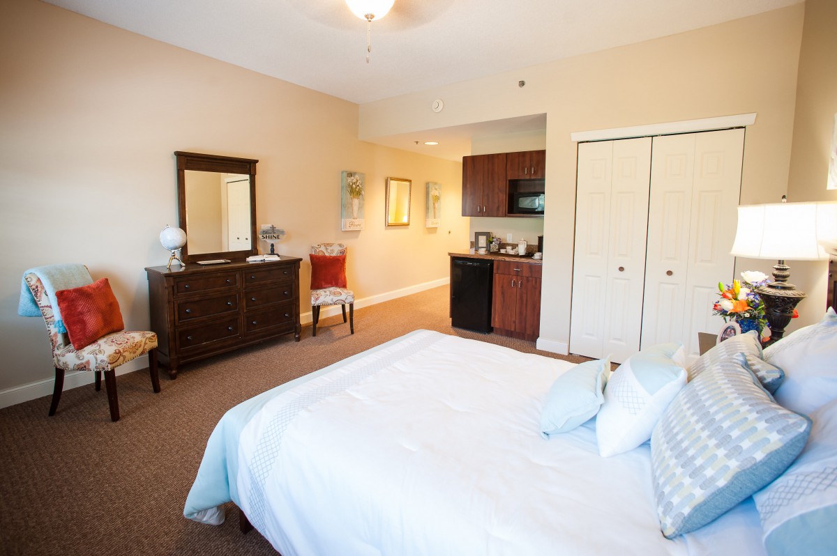 A cozy bedroom with a bed, dresser, and kitchenette.