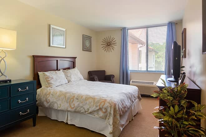 A cozy bedroom with a bed, chair, and window with curtains.