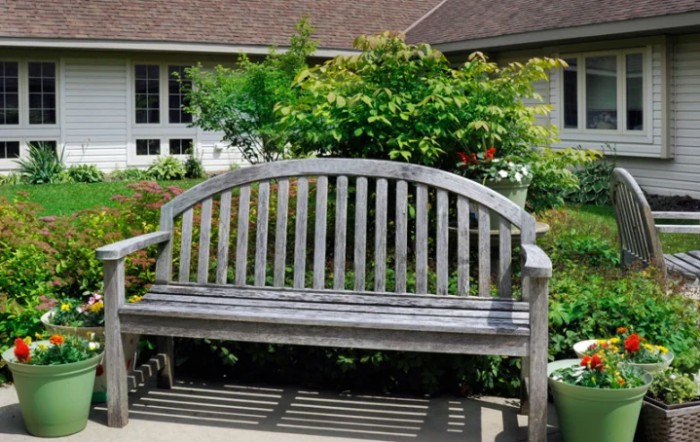 A wooden bench situated in a lush garden with a house in the background.