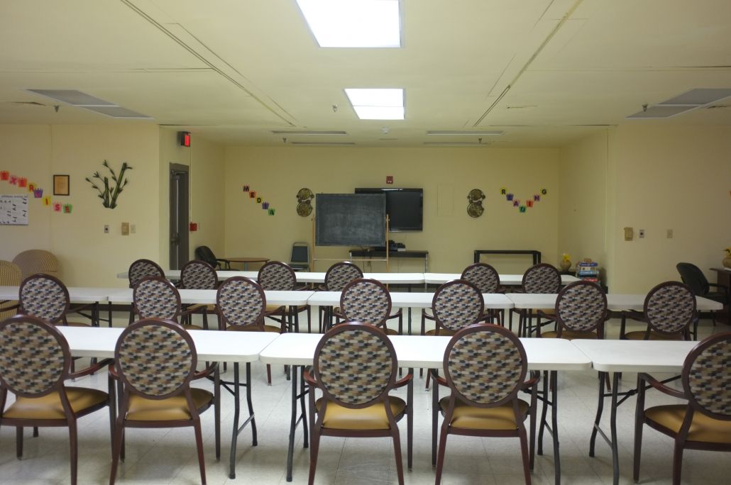 An empty classroom or meeting room with arranged tables and chairs facing a whiteboard.