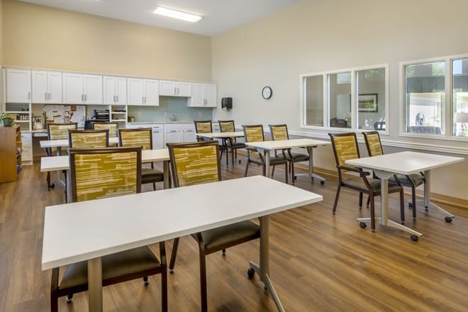 An empty classroom with tables and chairs arranged in rows on a wooden floor.