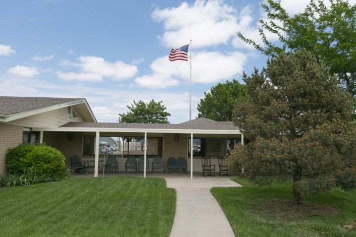 A building with an American flag flying on a flagpole, surrounded by a lawn and trees.