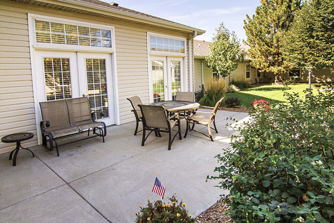 A sunny backyard patio with outdoor furniture and a small American flag in the garden.
