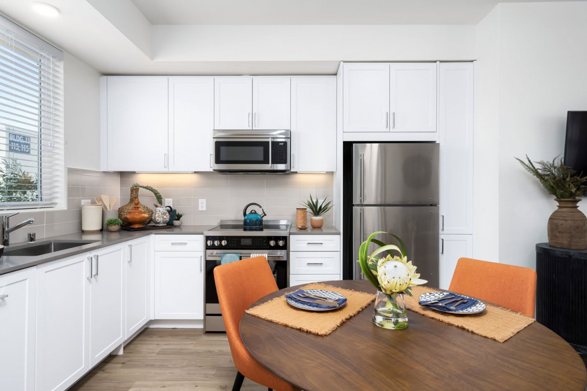 A modern kitchen with white cabinets, stainless steel appliances, and a dining table with orange chairs.