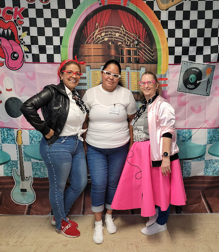 Three friends pose together in vibrant retro outfits, celebrating a fun event.