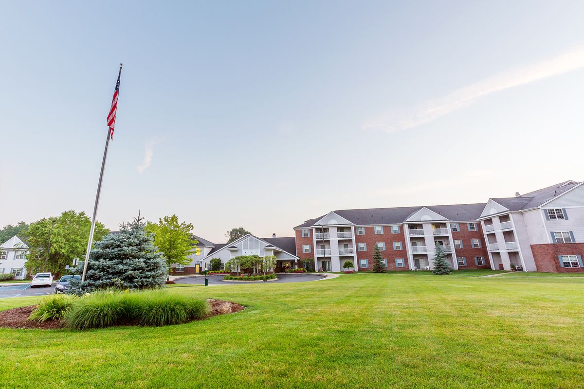 A scenic view of an apartment complex with a spacious lawn and a flagpole under a clear sky.