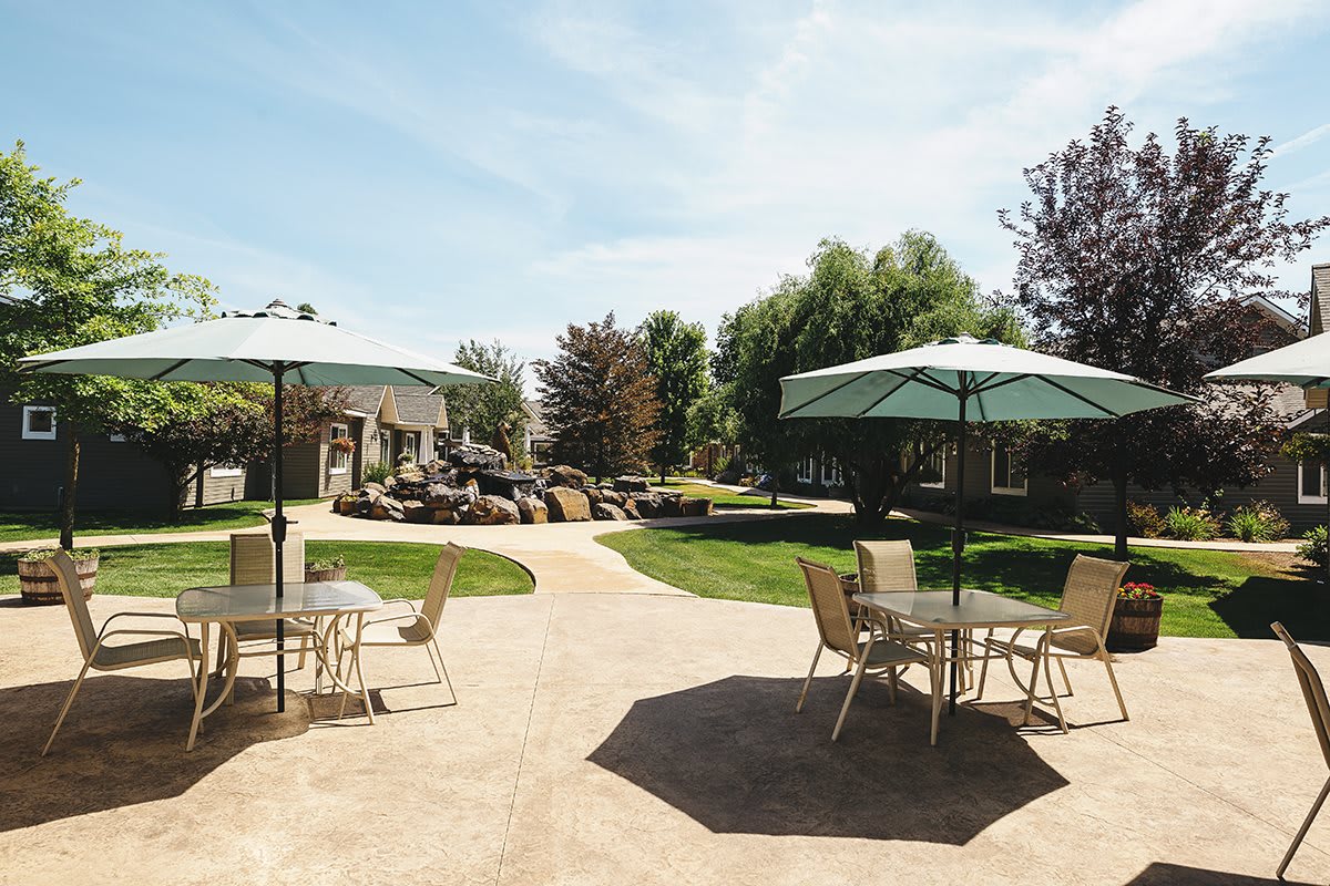 A serene outdoor patio area with tables, chairs, and umbrellas surrounded by a lush garden.