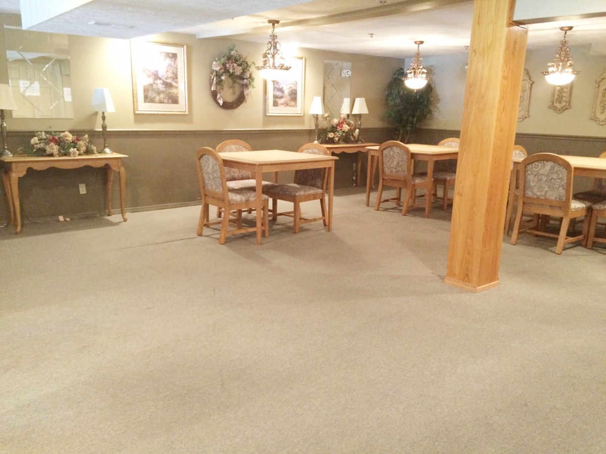 An indoor dining area with tables and chairs, featuring carpeted flooring and subtle wall decorations.