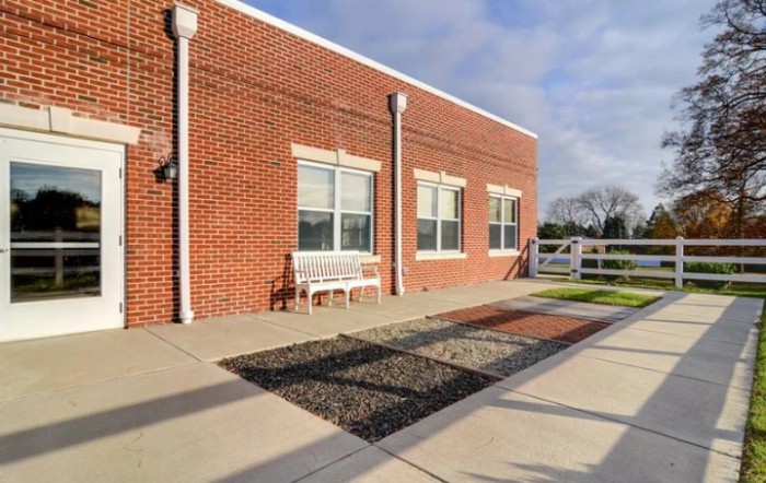 A brick building with large windows, a white bench, and a fenced area under a blue sky.