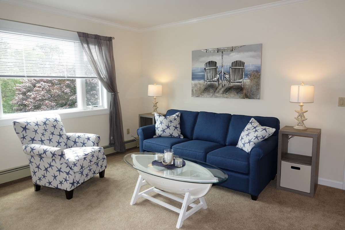 A cozy living room featuring a blue sofa, patterned armchair, and a glass-top coffee table.