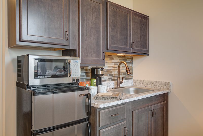 A compact kitchen area featuring dark wood cabinets, a stainless steel microwave, and a sink.