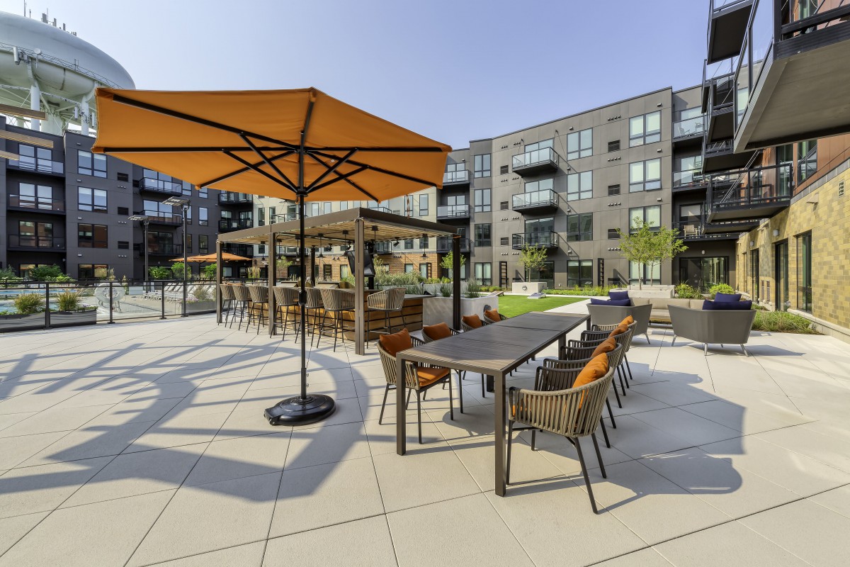 An outdoor patio with tables and chairs under large umbrellas, set within an apartment complex.