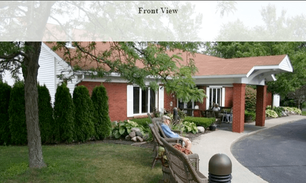 A front view of a red brick house with a garden and bench.