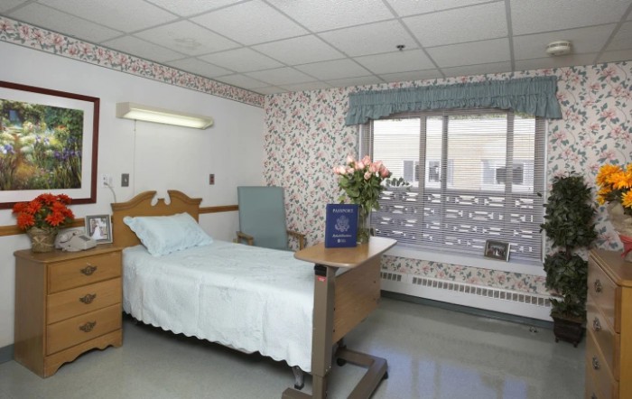 A clean and well-lit hospital room with a bed, table, and flowers by the window.