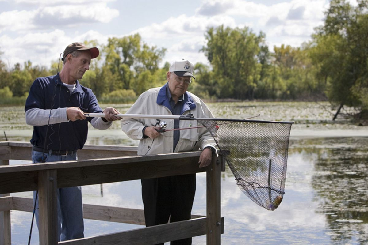 Two people fishing from a pier by a lake.