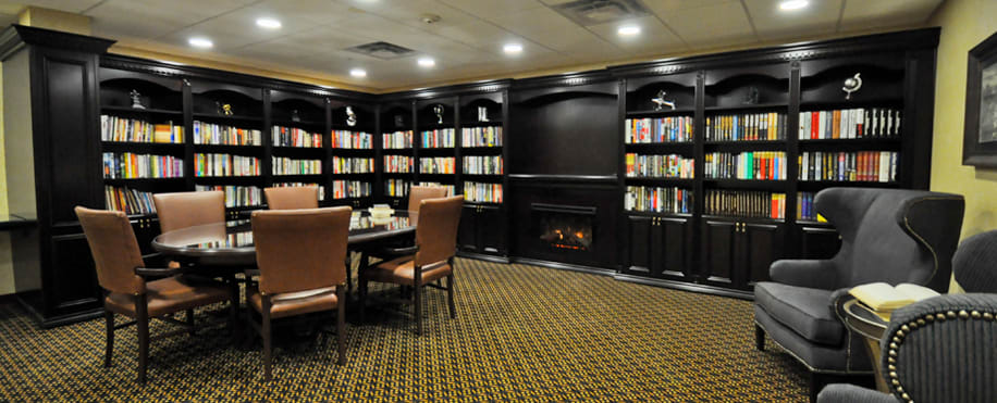 A cozy library room featuring bookshelves, a table with chairs, and a fireplace.