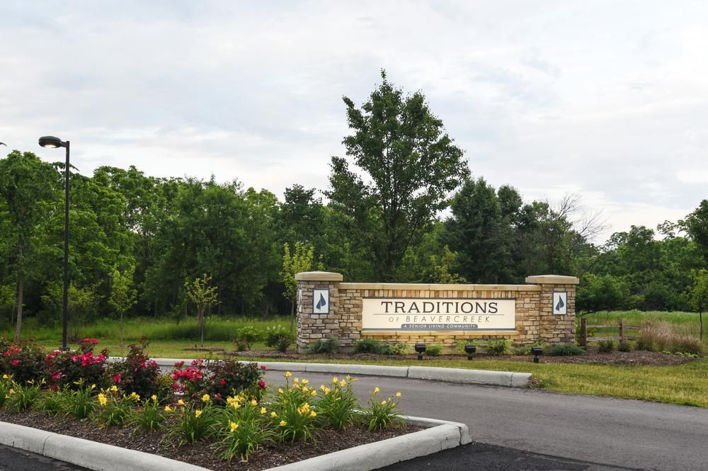Entrance sign for Traditions community surrounded by greenery and flowers.