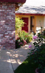 A charming garden pathway leads to a red door, surrounded by blooming flowers and greenery.