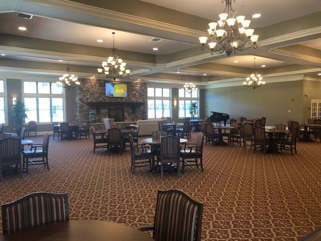 A spacious dining room with elegant chandeliers, multiple tables and chairs, a patterned carpet, large windows, and a fireplace.