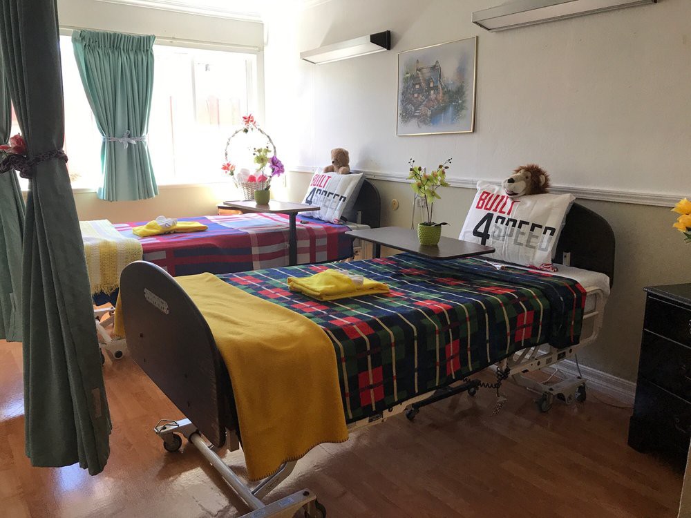 A bright hospital room with two decorated beds, featuring colorful blankets and flowers.