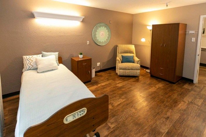 A cozy room featuring a hospital bed, armchair, and warm lighting.
