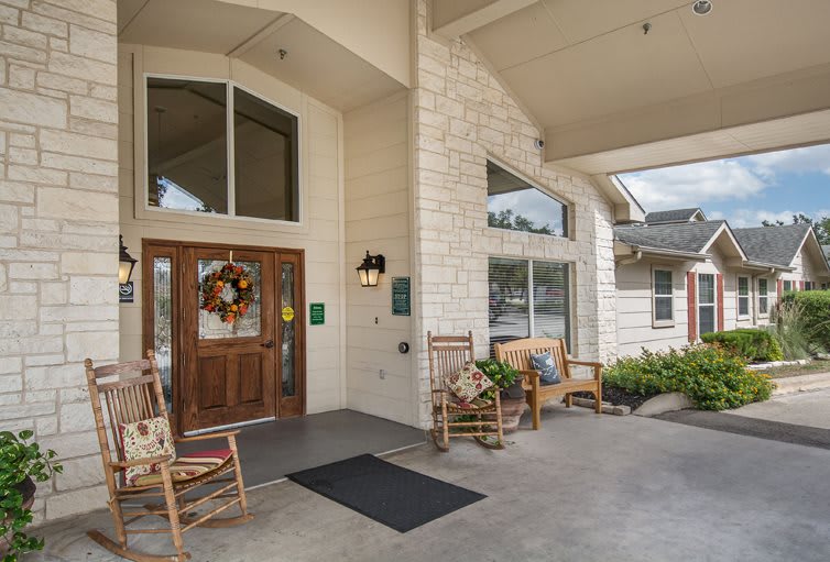 A welcoming building entrance with rocking chairs and a decorative wreath on the door.