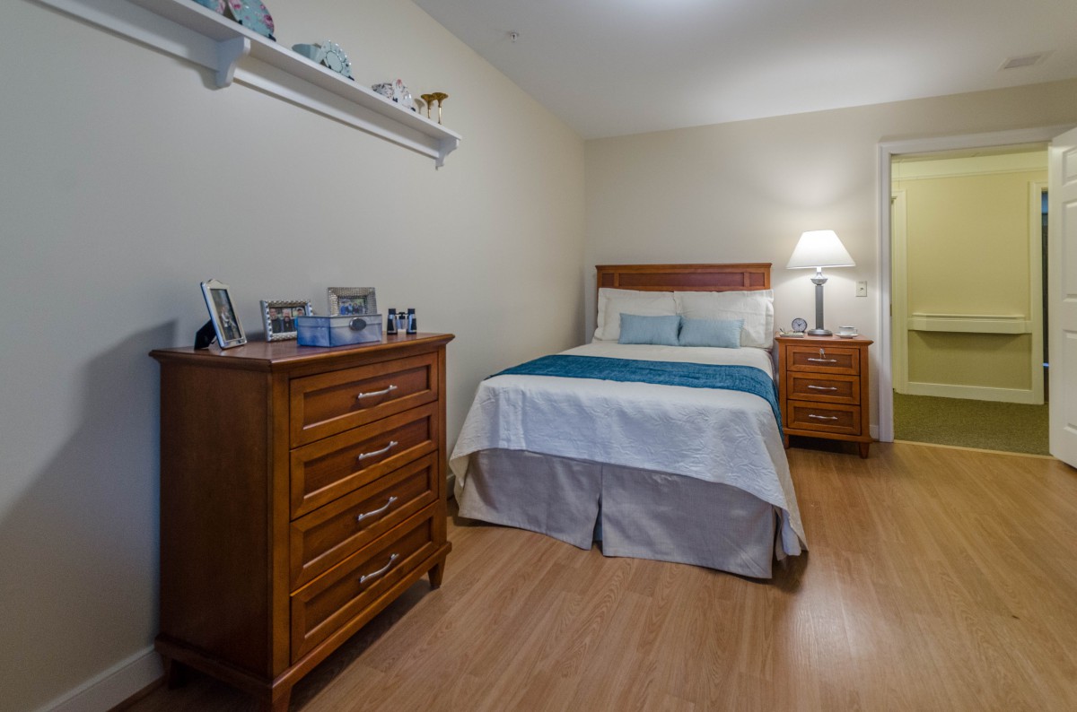 A cozy bedroom with wooden furniture and a neatly made bed, featuring a dresser adorned with framed photos.