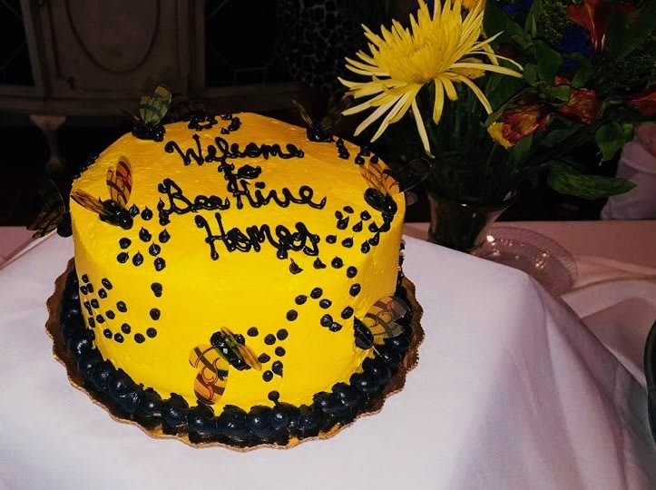 A vibrant yellow cake with bee decorations, accompanied by a flower arrangement.