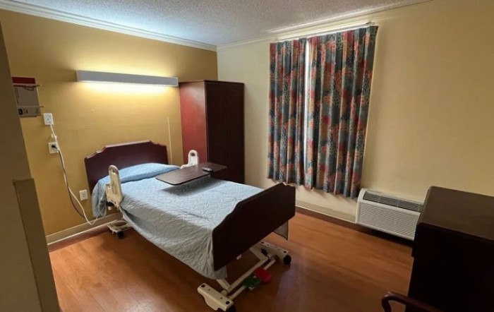 A hospital room with a single bed, wardrobe, and colorful curtains.