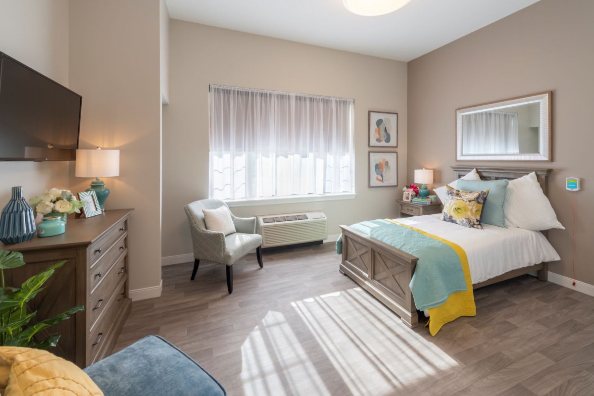 A cozy and well-lit bedroom with modern decor, featuring a bed, chair, and large window.