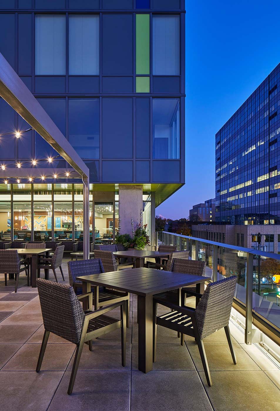 A modern rooftop patio with tables and chairs overlooking the city at dusk.