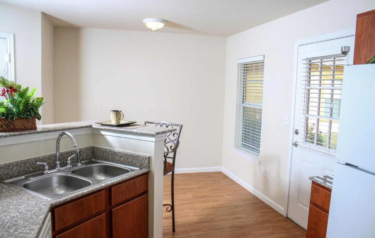 A bright kitchen area with a sink, countertop, and wooden flooring.