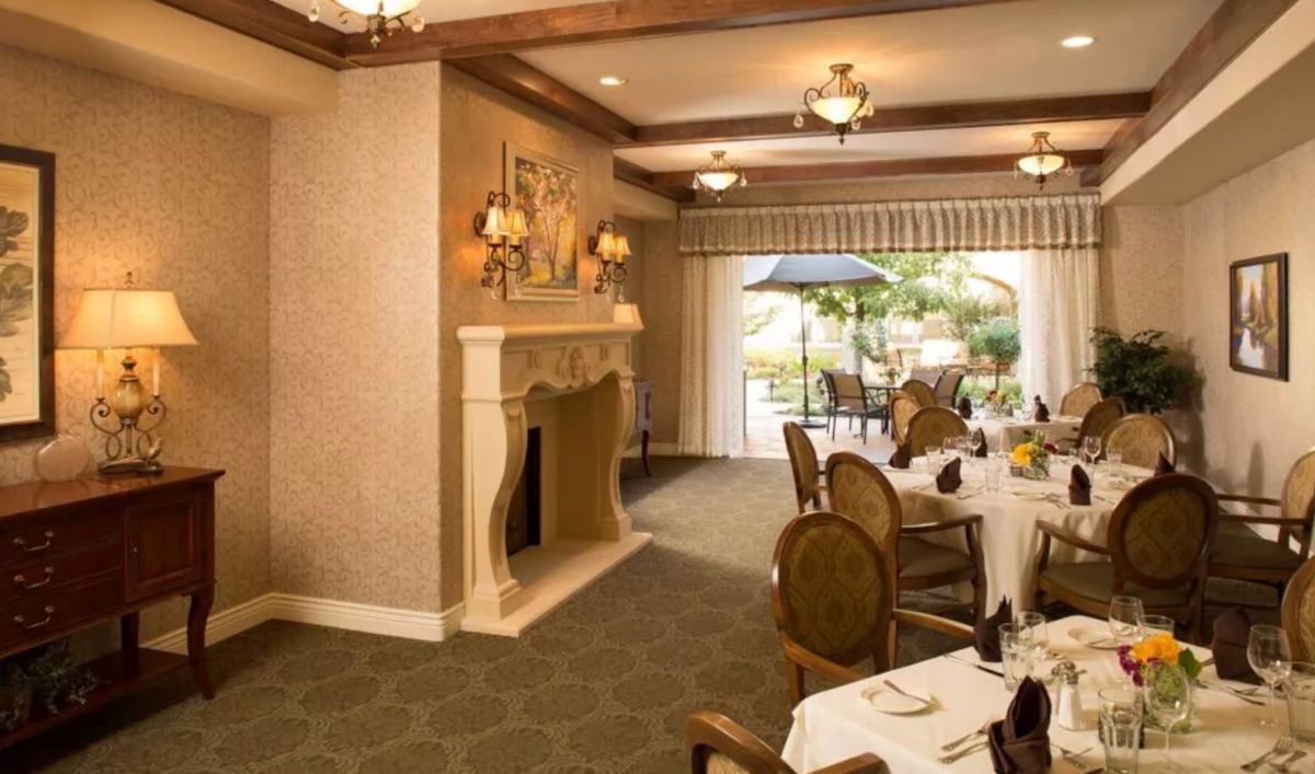 An elegant dining room with a fireplace and chandelier, offering a view of the outdoor patio.