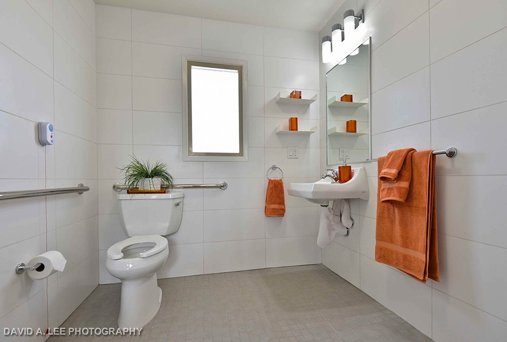 A modern bathroom with white walls and orange accents features a wall-mounted sink and mirror.