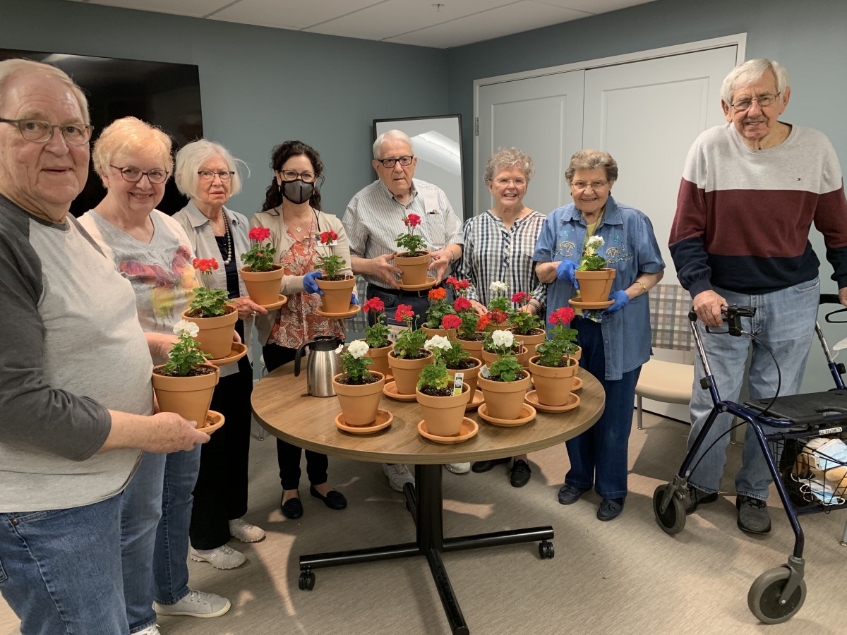 A group of seniors proudly display their potted flowers around a table indoors.
