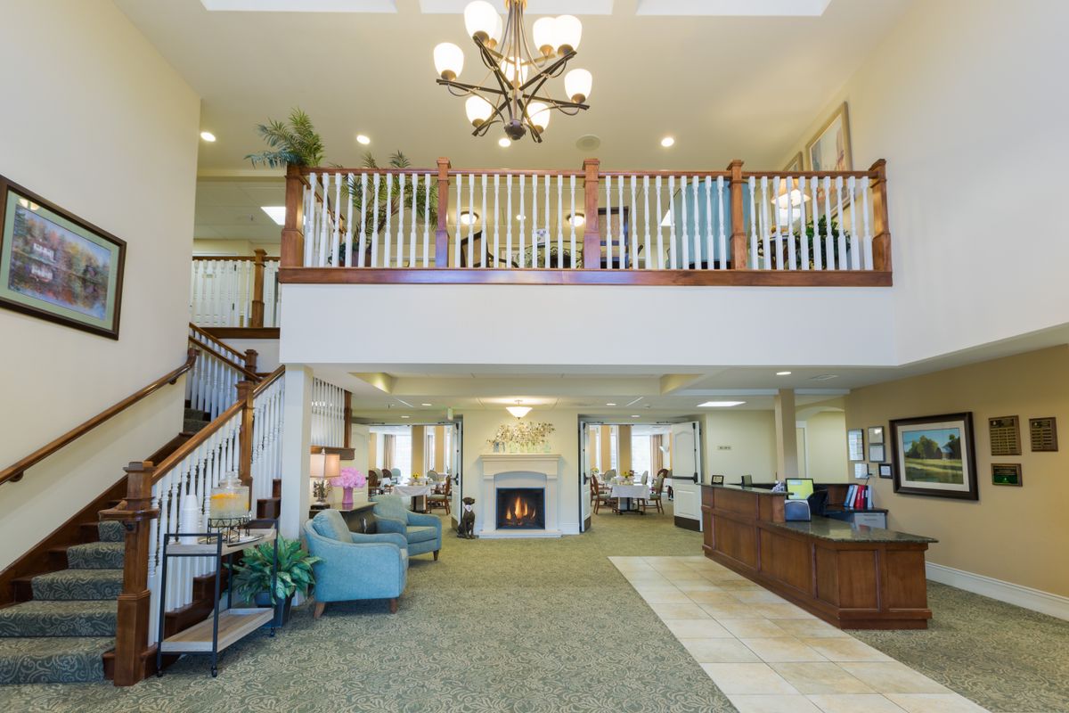 A spacious hotel lobby featuring a central fireplace, elegant chandelier, and comfortable seating areas with a balcony overlooking the space.