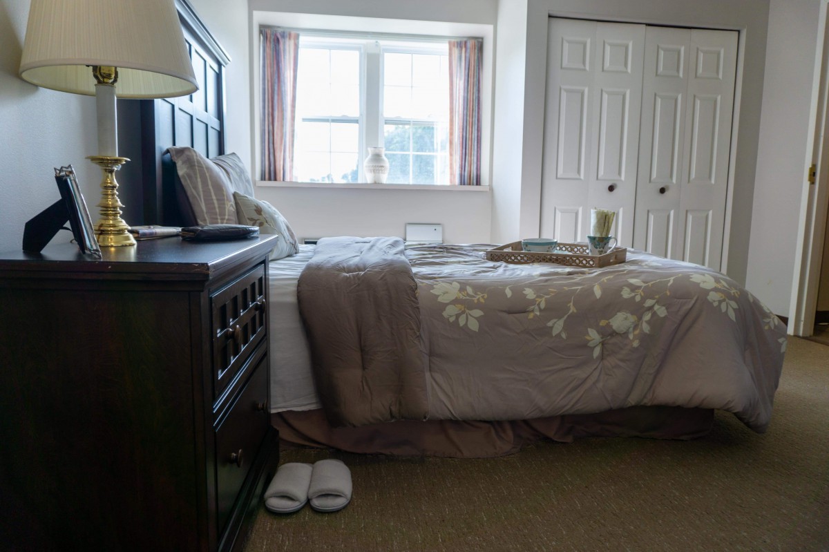 A cozy bedroom with a neatly made bed and slippers on the floor.