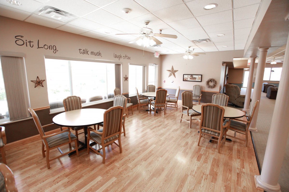 A spacious dining room with wooden floors, several tables and chairs, and large windows letting in natural light.
